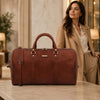 Leather Travel Duffel Bag in brown leather with woman in fashionable outfit in elegant setting.