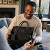 Man smiling while receiving a Leather Travel Gift Set, including a duffle bag, toiletry bag, and passport cover.