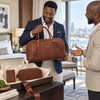 Man holding Leather Travel Gift Set in hotel room, showcasing duffle bag, toiletry bag, and passport cover.