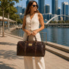 Woman in sunglasses carrying a stylish Weekender Travel Bag beside a waterfront in an urban setting.