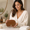 Woman holding a Luxury Soft Leather Toiletry Case at a bathroom counter with candles and skincare products.