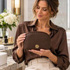 Woman holding the Luxury Soft Leather Toiletry Case in chocolate pebbled leather with a gold-tone zipper and logo.