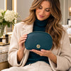 Woman holding the Luxury Soft Leather Toiletry Case in teal pebbled leather with a gold-tone zipper and logo.