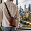 Man wearing a leather Crossbody Bag Mens, standing by a window with a city skyline view.