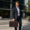 Man in a suit holding an Mens Leather Messenger Bag while walking outdoors.