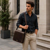 Stylish man holding a Leather Laptop Messenger Bag while walking outside in an urban setting.