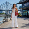 Woman wearing a stylish outfit carrying a red Leather Bucket Bag near the waterfront.