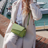 Shoulder Bag For Ladies in green worn with a cream coat, set against a marina backdrop with boats.