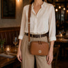 Woman wearing a small leather crossbody bag, styled with a chic outfit in a cozy restaurant setting.