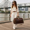 Woman holding a Small Leather Trolley Bag near a river with a city skyline in the background.