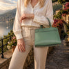 Elegant woman holding a Small Tote Bag in mint green by a scenic lakeside location.