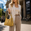 Woman in a blazer holding a pastel yellow Soft Leather Handbag in front of the National Gallery of Victoria.