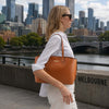Woman wearing Soft Leather Shopper Bag while walking in an urban setting with skyscrapers in the background.