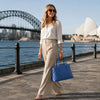 Woman wearing beige trousers and a white shirt walking with a Azure Quilted Leather Handbag in front of Sydney Opera House.