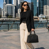 Woman in a black blazer and sunglasses holding a Quilted Leather Handbag while walking in the city.