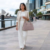 Woman in a light suit walking by the water, carrying a Quilted Leather Handbag, stylishly dressed.