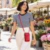 A woman walking outdoors in a real market setting, wearing a navy and white striped short-sleeve top, cream pants, and the lipstick red Wallet And Mobile Phone Holder