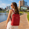 Woman wearing a lipstick red Leather Backpack Ladies while walking by a waterfront in a sunny urban setting.