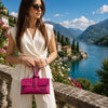 Woman in a white outfit holding a pink Womens Leather Clutch by a scenic lake with mountains in the background.