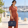 Woman in rust-colored jumpsuit holding a Womens Leather Shopper Bag by the waterfront.