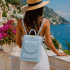 Womens Small Backpack in light blue worn by a woman on a scenic coastal backdrop, perfect for stylish daily use.