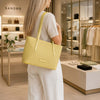 Woman in a store carrying a pastel yellow Woven Leather Shopping Bag from Sandro, showcasing stylish fashion accessories.