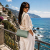 Woven Leather Shoulder Bag showcased with a model against a scenic coastal backdrop, highlighting its elegant design.