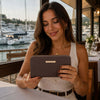Smiling woman holding a Zipper Wallet at a waterfront restaurant.